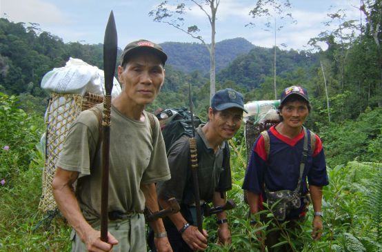 Três homens indígenas com cestas nas costas na floresta tropical malaia
