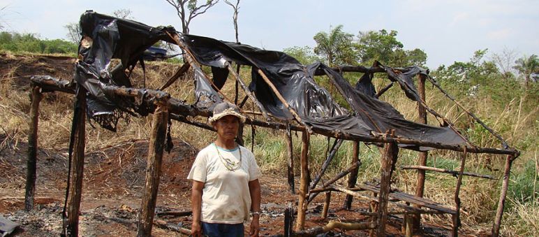 Damiana, uma Guarani-Kaiowá e líder religioso do Apyka'y, diante de uma cabana queimada depois da evicção forçada Um Guarani-Kaiowá à frente da sua casa