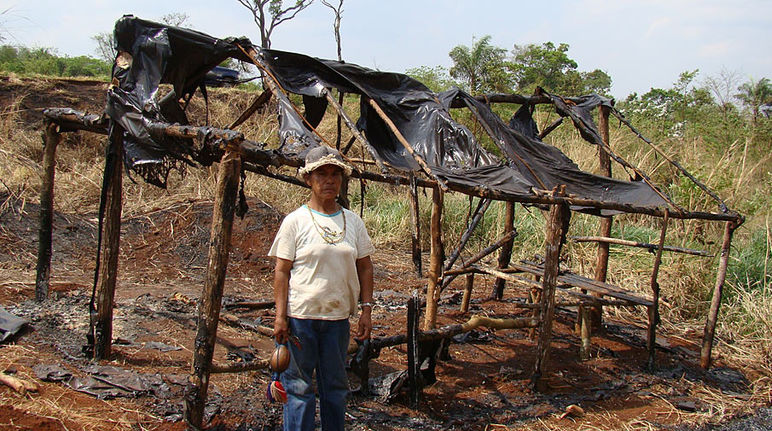 Damiana, uma guarani-kaiowá e líder religiosa dos apyka'y, em frente de uma cabana incendiada depois de expulsões forçadas Um Guarani-Kaiowá à frente da sua casa