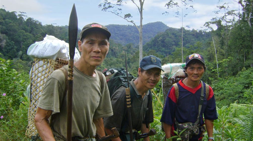 Três homens indígenas com cestas nas costas na floresta tropical malaia